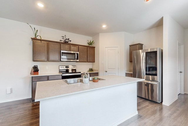 kitchen featuring wood-type flooring, ceiling fan, range with electric stovetop, a center island with sink, and refrigerator