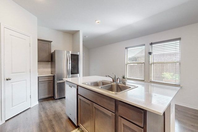 kitchen with stainless steel appliances, hardwood / wood-style floors, sink, dark brown cabinets, and a kitchen island with sink