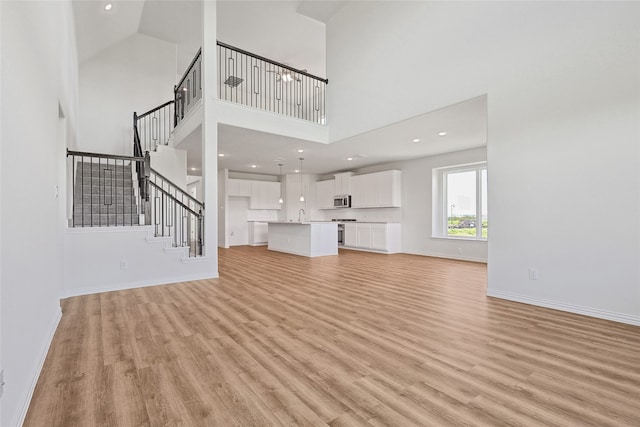 unfurnished living room featuring high vaulted ceiling and light wood-type flooring