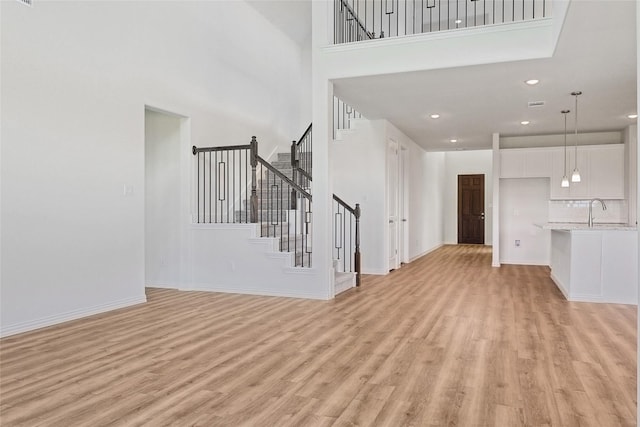 unfurnished living room featuring sink, a towering ceiling, and light hardwood / wood-style floors