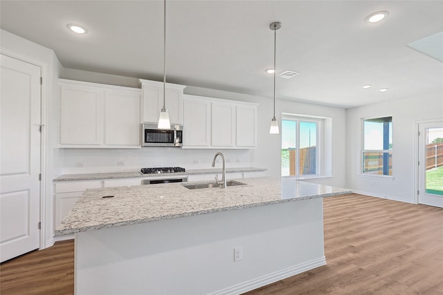 kitchen featuring sink, light stone counters, hanging light fixtures, a kitchen island with sink, and white cabinets