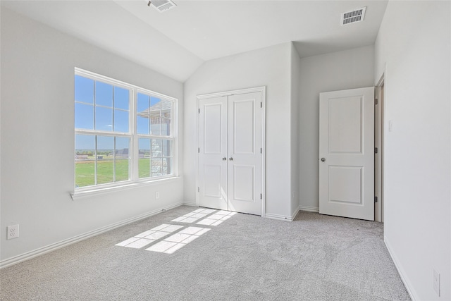 unfurnished bedroom with light carpet, a closet, and lofted ceiling