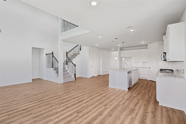 kitchen featuring white cabinets, a center island with sink, appliances with stainless steel finishes, light wood-type flooring, and decorative backsplash