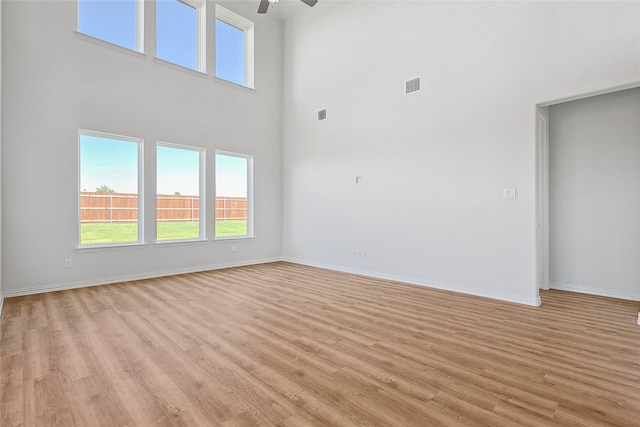 unfurnished living room with a towering ceiling, light hardwood / wood-style flooring, and ceiling fan