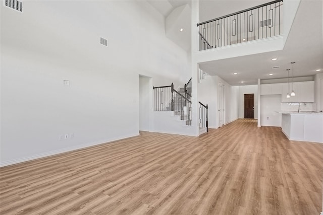 unfurnished living room featuring light wood-type flooring, a towering ceiling, and sink