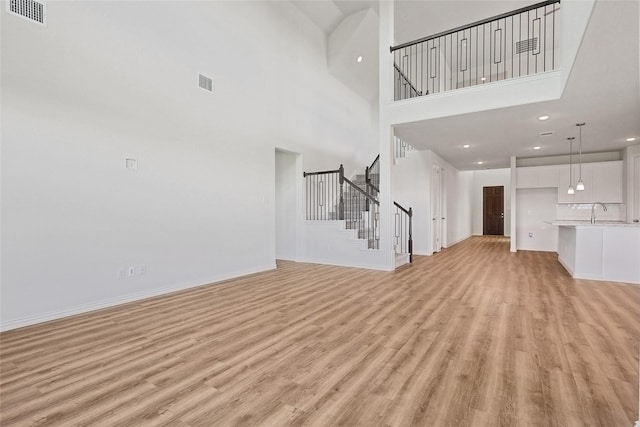 unfurnished living room with a high ceiling, sink, and light hardwood / wood-style flooring