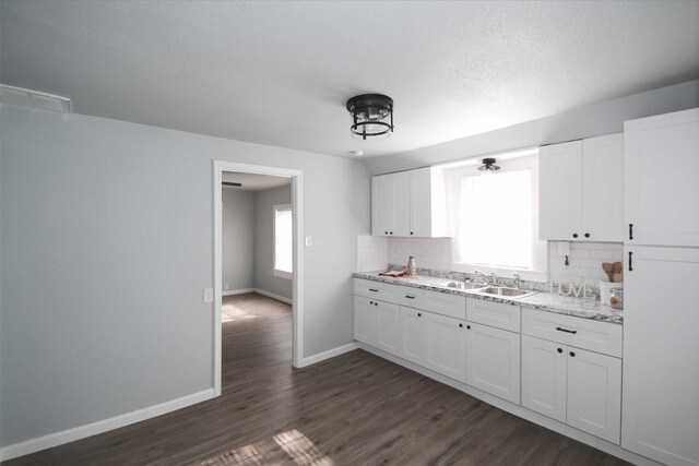 kitchen featuring sink, decorative backsplash, light stone countertops, white cabinetry, and dark hardwood / wood-style flooring