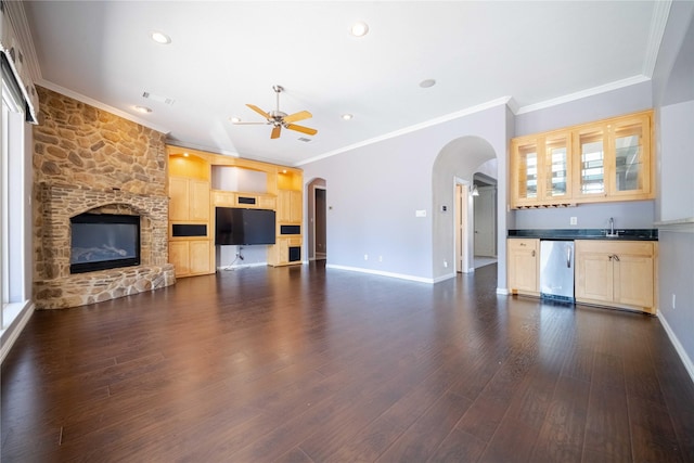 living room with sink, a stone fireplace, ornamental molding, and dark hardwood / wood-style floors