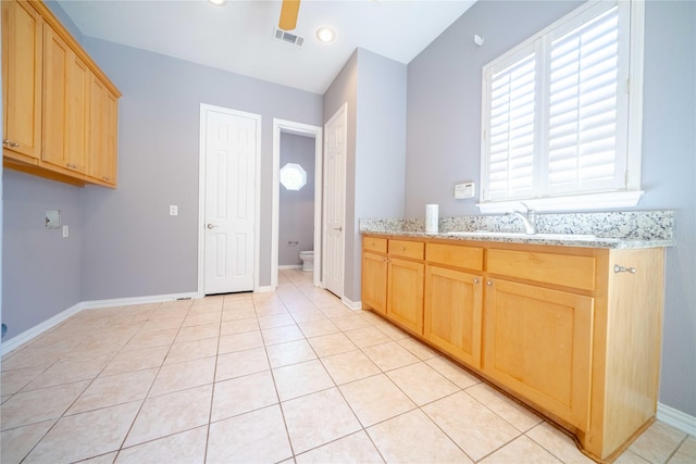 kitchen with light tile patterned floors, sink, ceiling fan, light stone countertops, and light brown cabinetry