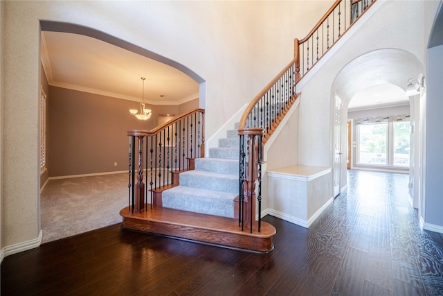 stairway featuring hardwood / wood-style flooring, ornamental molding, a chandelier, and a high ceiling