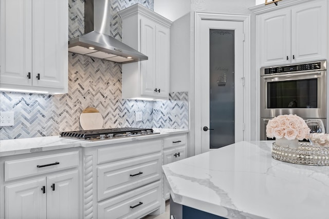 kitchen with wall chimney range hood, decorative backsplash, white cabinets, and appliances with stainless steel finishes