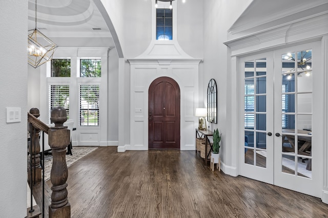 foyer with dark wood-type flooring, crown molding, a raised ceiling, and a towering ceiling