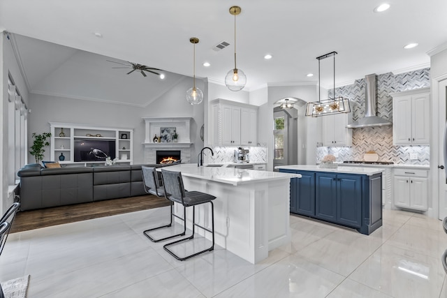 kitchen with wall chimney range hood, blue cabinets, a large island, pendant lighting, and white cabinets