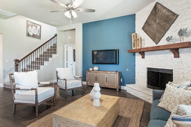 living room featuring ceiling fan, dark hardwood / wood-style floors, and a stone fireplace