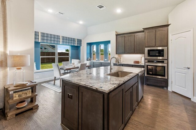 kitchen featuring vaulted ceiling, appliances with stainless steel finishes, sink, light stone countertops, and dark brown cabinets