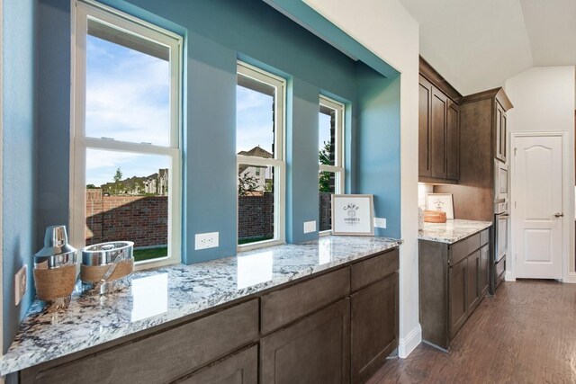 kitchen featuring appliances with stainless steel finishes, dark brown cabinets, dark hardwood / wood-style floors, light stone counters, and vaulted ceiling