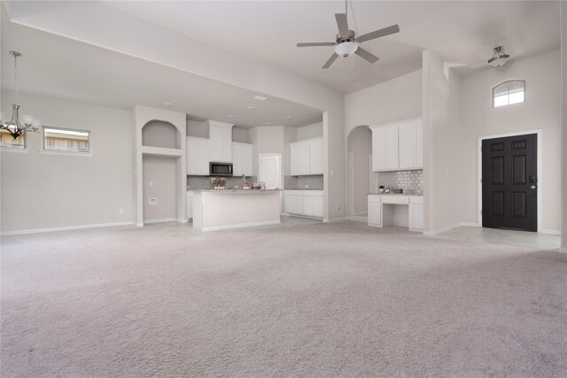 unfurnished living room featuring ceiling fan with notable chandelier, a towering ceiling, and light colored carpet