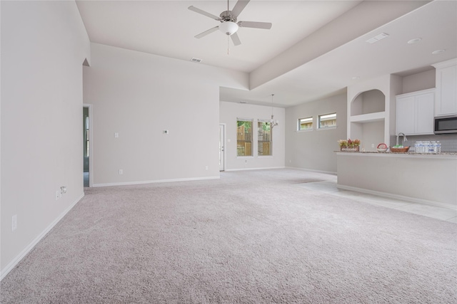 unfurnished living room featuring built in shelves, ceiling fan with notable chandelier, and light colored carpet