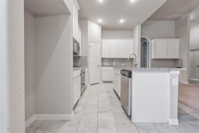 kitchen with sink, appliances with stainless steel finishes, a kitchen island with sink, white cabinetry, and light stone counters