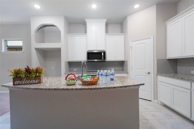 kitchen with an island with sink, white cabinets, light stone counters, and decorative backsplash