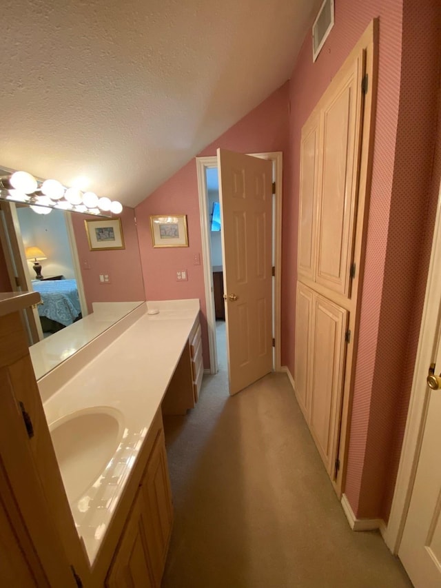 ensuite bathroom featuring connected bathroom, vaulted ceiling, vanity, a textured ceiling, and visible vents