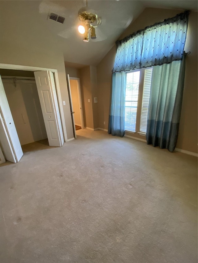 unfurnished bedroom with a closet, visible vents, ceiling fan, vaulted ceiling, and light colored carpet