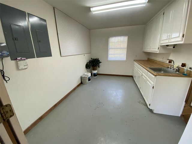 kitchen with finished concrete flooring, white cabinets, electric panel, baseboards, and a sink