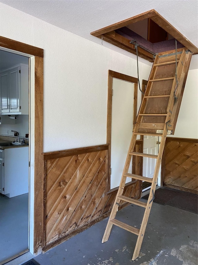 stairs featuring concrete floors, wooden walls, and wainscoting