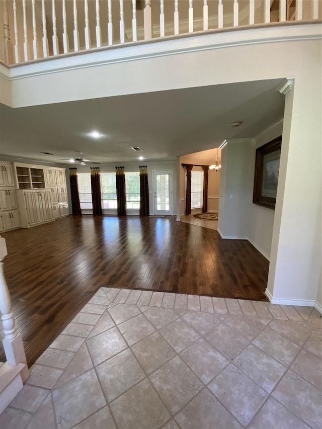unfurnished living room with tile patterned floors, a high ceiling, baseboards, ornamental molding, and an inviting chandelier