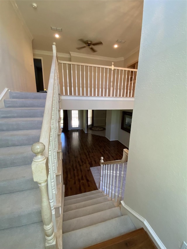 staircase featuring crown molding, baseboards, visible vents, a ceiling fan, and wood finished floors