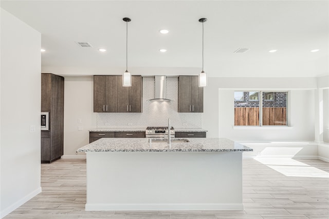 kitchen with sink, wall chimney range hood, a kitchen island with sink, and light stone counters