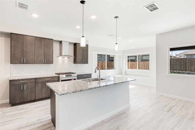 kitchen featuring decorative light fixtures, sink, dark brown cabinetry, wall chimney range hood, and stainless steel gas range