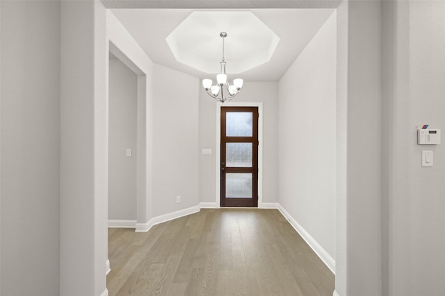 entrance foyer featuring a notable chandelier, light hardwood / wood-style flooring, and a raised ceiling