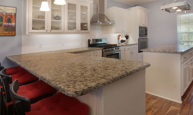 kitchen with hanging light fixtures, a kitchen breakfast bar, gas stove, and wall chimney exhaust hood