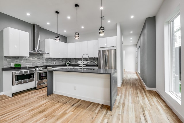 kitchen featuring sink, white cabinetry, hanging light fixtures, appliances with stainless steel finishes, and wall chimney range hood