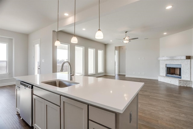 kitchen with dishwasher, sink, a stone fireplace, an island with sink, and decorative light fixtures