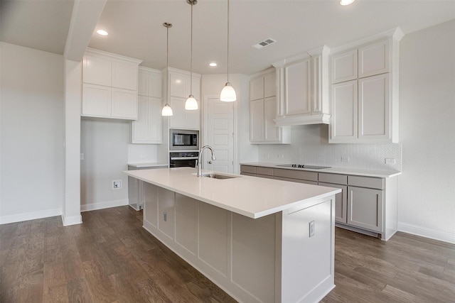 kitchen with black electric stovetop, built in microwave, sink, a center island with sink, and oven