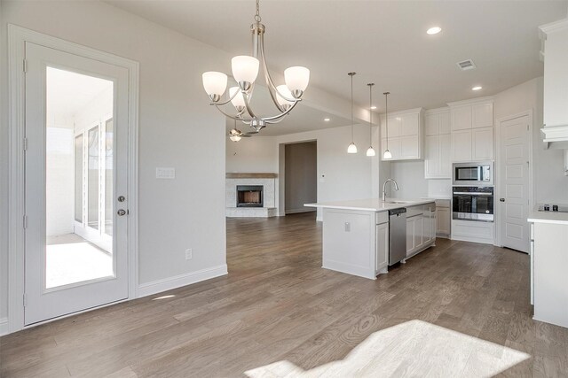 kitchen with white cabinetry, sink, stainless steel appliances, decorative light fixtures, and a kitchen island with sink