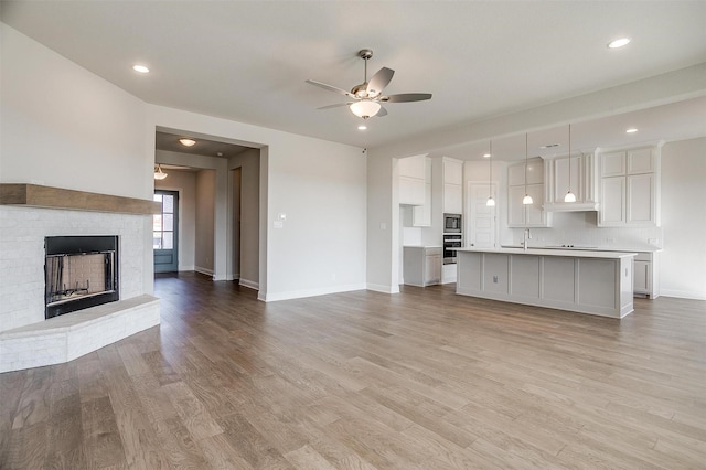 unfurnished living room featuring ceiling fan, sink, light wood-type flooring, and a fireplace