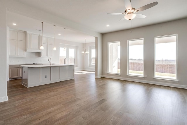 kitchen featuring tasteful backsplash, ceiling fan with notable chandelier, decorative light fixtures, a center island with sink, and dark hardwood / wood-style floors