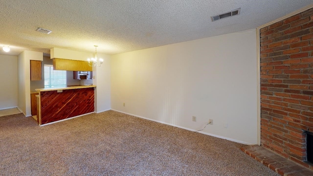 unfurnished living room featuring an inviting chandelier, carpet floors, a textured ceiling, a brick fireplace, and brick wall