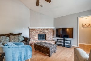 living room featuring a brick fireplace, wood-type flooring, lofted ceiling, and ceiling fan