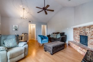 living room featuring lofted ceiling, light hardwood / wood-style floors, ceiling fan with notable chandelier, and a brick fireplace