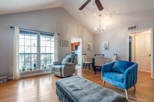 living room with high vaulted ceiling, ceiling fan with notable chandelier, and hardwood / wood-style flooring