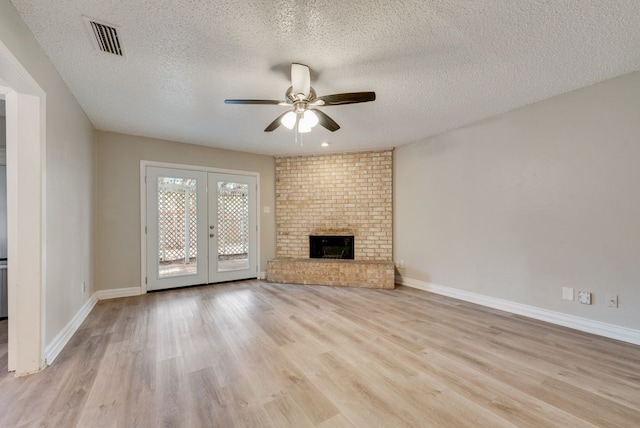 unfurnished living room featuring ceiling fan, light hardwood / wood-style floors, a textured ceiling, a brick fireplace, and french doors