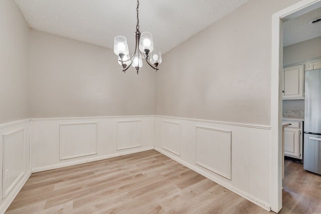 unfurnished dining area featuring a chandelier, a textured ceiling, and light wood-type flooring