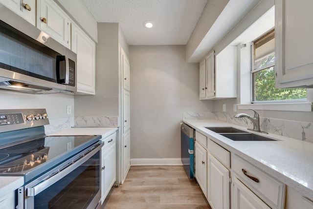 kitchen with sink, light hardwood / wood-style flooring, a textured ceiling, appliances with stainless steel finishes, and white cabinets