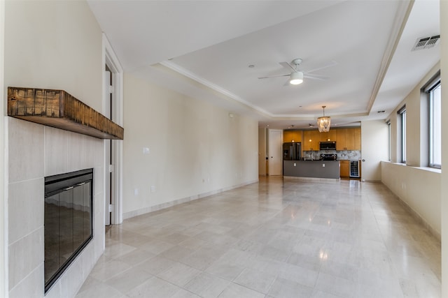 unfurnished living room with light tile patterned floors, a raised ceiling, ceiling fan, ornamental molding, and a tiled fireplace