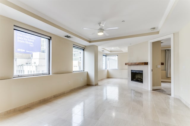 unfurnished living room featuring ceiling fan, ornamental molding, light tile patterned flooring, a fireplace, and a tray ceiling