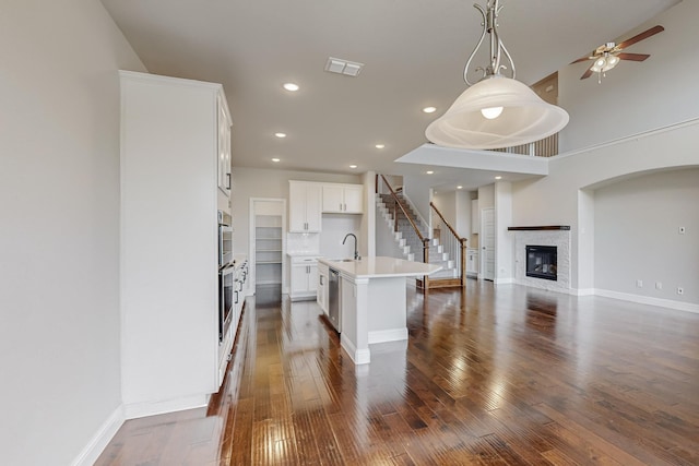 kitchen featuring dark hardwood / wood-style floors, decorative light fixtures, white cabinets, a kitchen island with sink, and stainless steel dishwasher